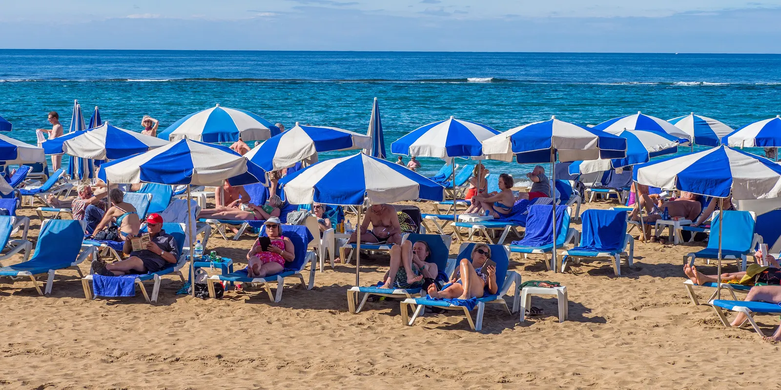 Is Gran Canaria veilig? Zonnende badgasten onder parasols op Playa de las Canteras in Las Palmas de Gran Canaria