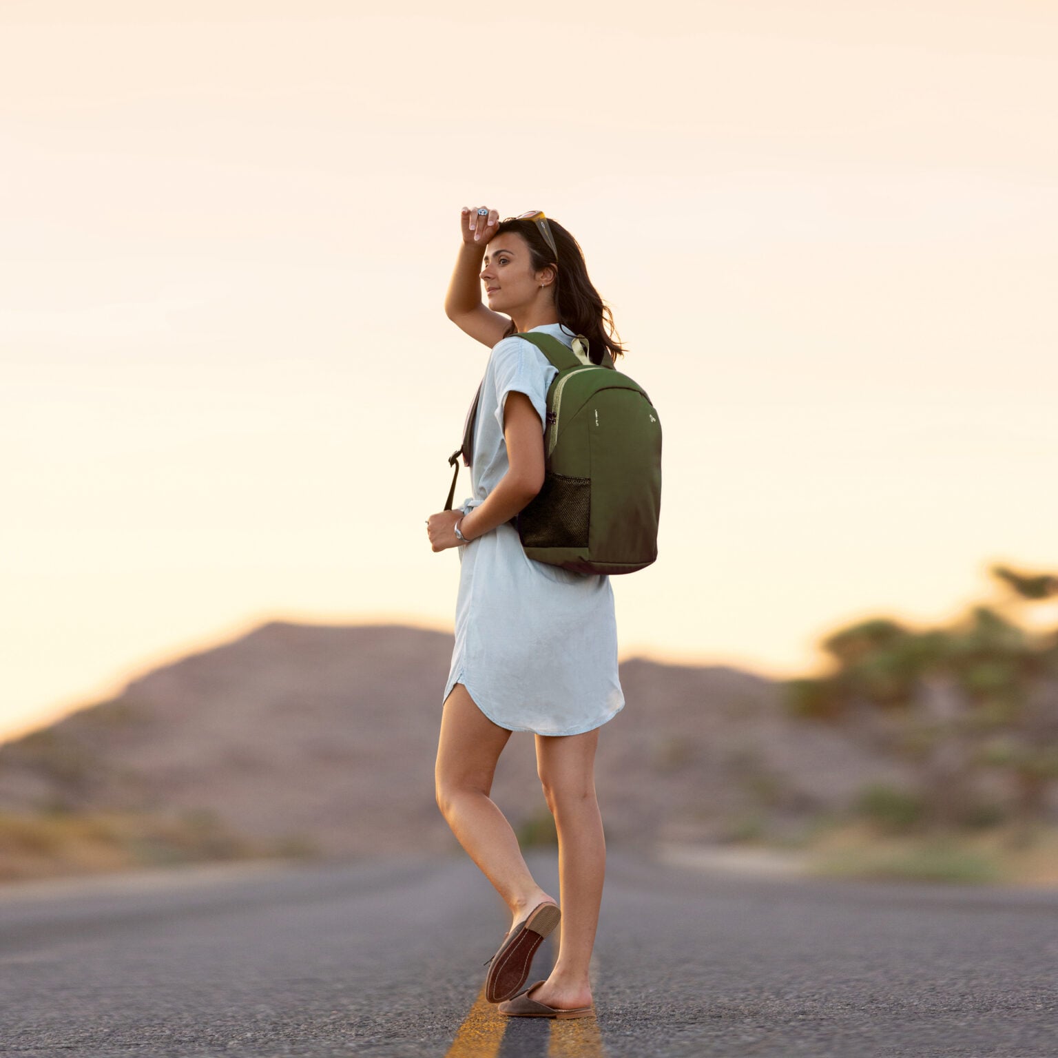 Vrouw draagt de Travelon Voyages daypack in olijfgroen op een weg bij zonsondergang