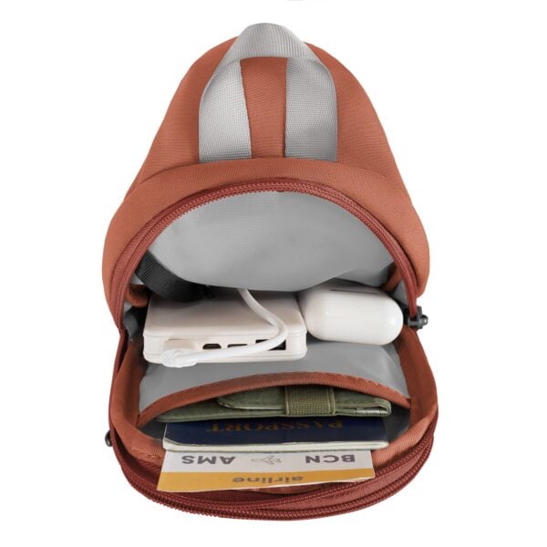 Geopende Travelon Voyages compact sling in koraal met powerbank, portemonnee, paspoort en instapkaarten
