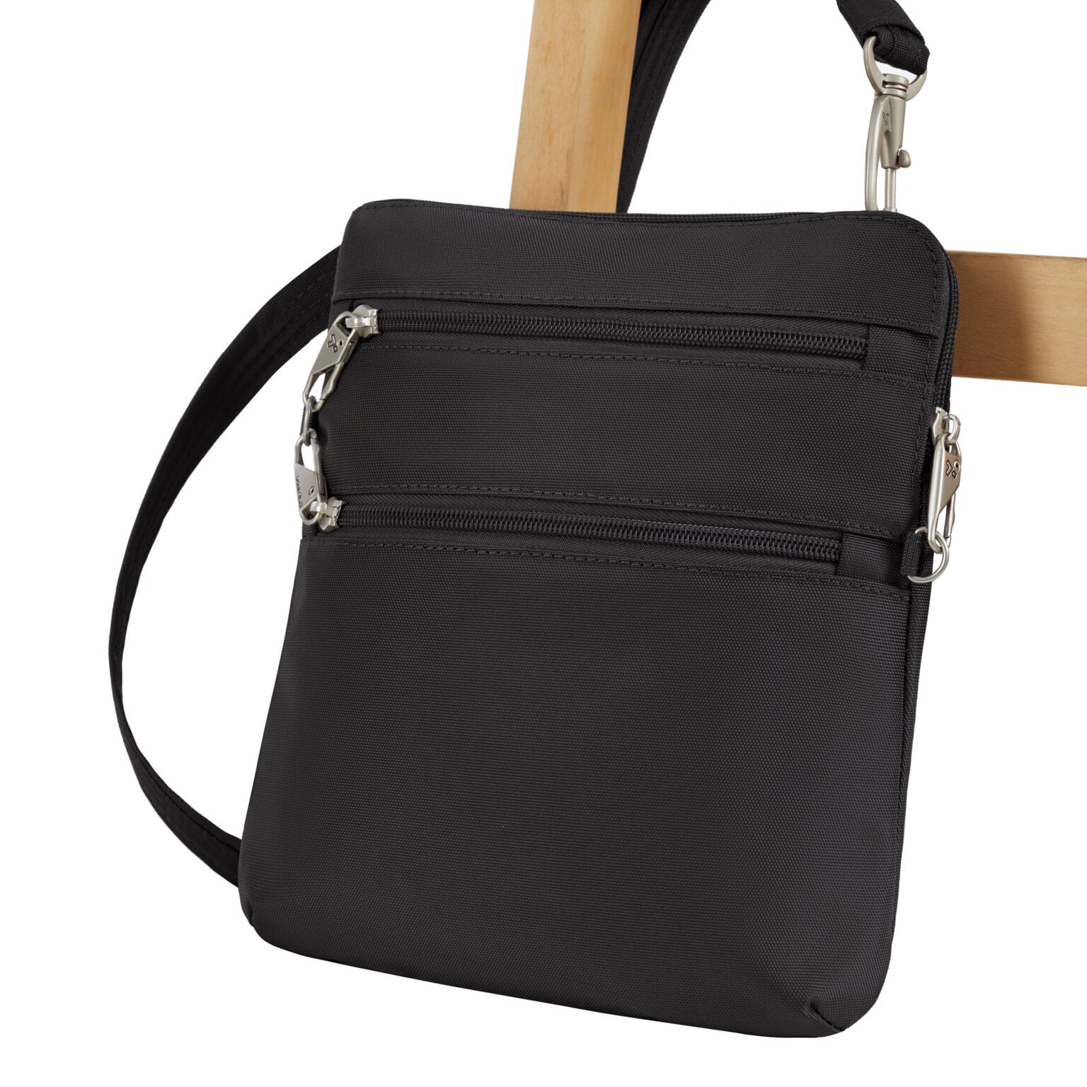 De Travelon Classic slanke crossbody tas in zwart vastgezet aan de poot van een stoel