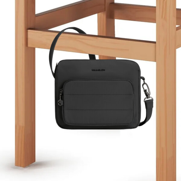 De Travelon Roam brede crossbody tas in zwart vastgezet aan de poot van een stoel